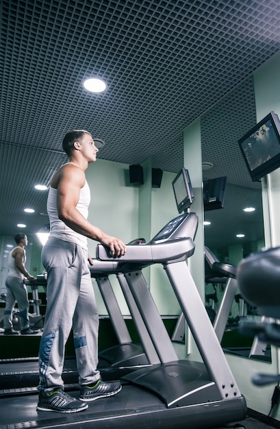 Jovem homem musculoso na pista na academia assistindo tv