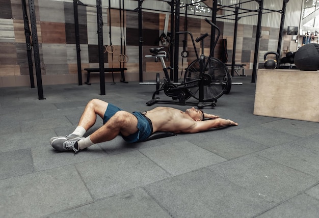 Jovem homem musculoso praticando alongamento muscular no clube de saúde moderno