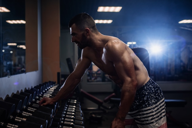 Foto jovem homem musculoso treina as costas com halteres no ginásio