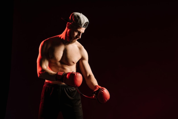 Jovem homem musculoso usando luvas de boxe no fundo do estúdio