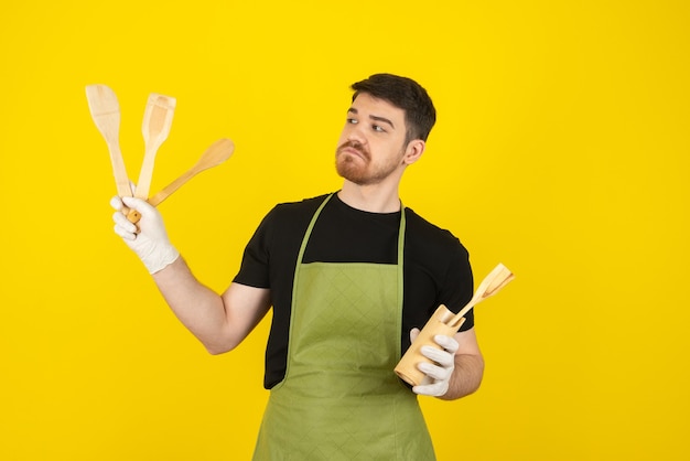 Jovem homem pensativo segurando colheres de madeira em amarelo.