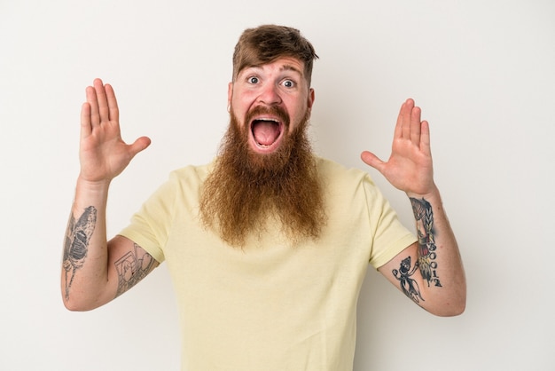 Jovem homem ruivo, caucasiano, com barba comprida, isolado no fundo branco, comemorando uma vitória ou sucesso, ele fica surpreso e chocado.