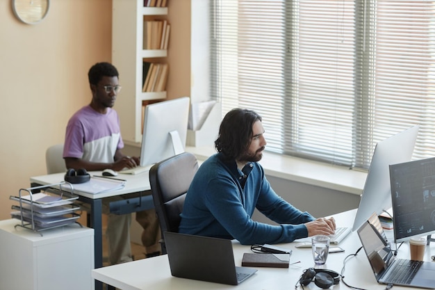 Foto jovem homem sério pressionando as teclas do teclado do computador no local de trabalho