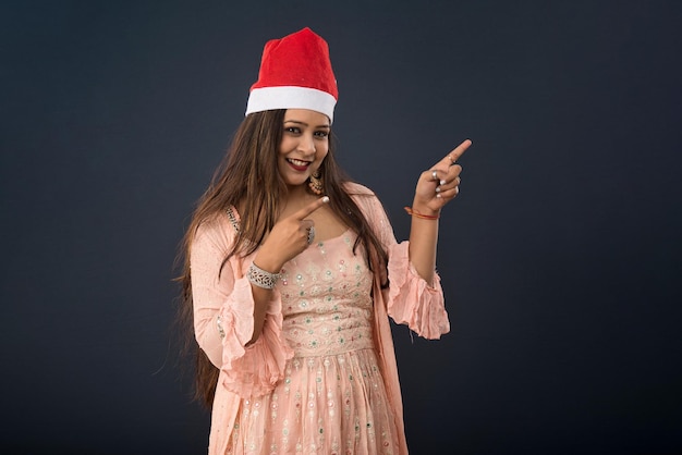 Jovem indiana celebrando o natal sorrindo e apontando algo para um espaço em branco no conceito de natal de fundo cinza