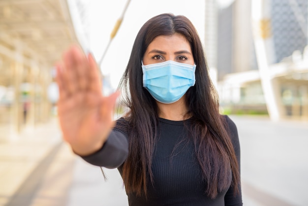 Foto jovem indiana com máscara para proteção contra surto do vírus corona, mostrando gesto de parada na cidade