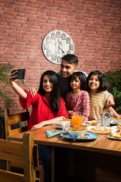 Jovem indiana Família de quatro pessoas comendo comida na mesa de jantar em casa ou no restaurante. Mãe, pai e duas filhas do sul da Ásia comendo juntos
