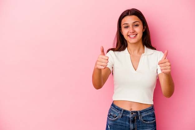 Jovem indiana isolada na parede rosa sorrindo e levantando o polegar