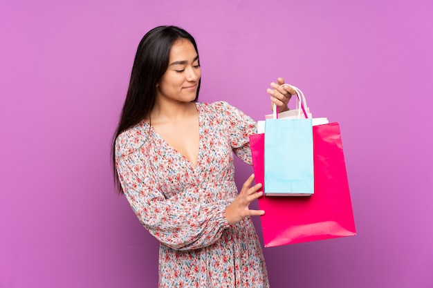 Jovem indiana isolada na parede roxa segurando sacolas de compras