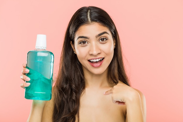 Jovem indiana segurando uma garrafa de colutório surpreendeu apontando para si mesmo, sorrindo amplamente.