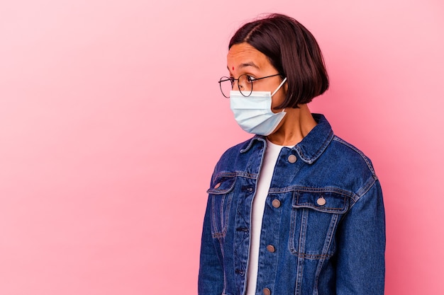 Jovem indiana usando uma máscara antivírus isolada em rosa, em choque por causa de algo que viu.