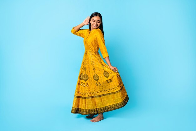 Jovem indiana usando vestido tradicional amarelo dançando fundo azul