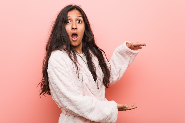 Jovem indiana vestindo pijama chocado e espantado, segurando um espaço de cópia entre as mãos.