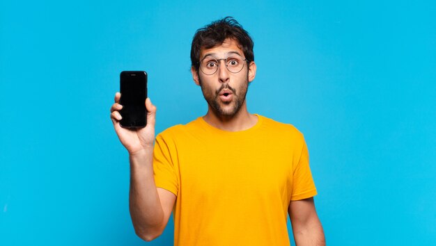 Jovem indiano bonito com expressão de medo e segurando um telefone celular