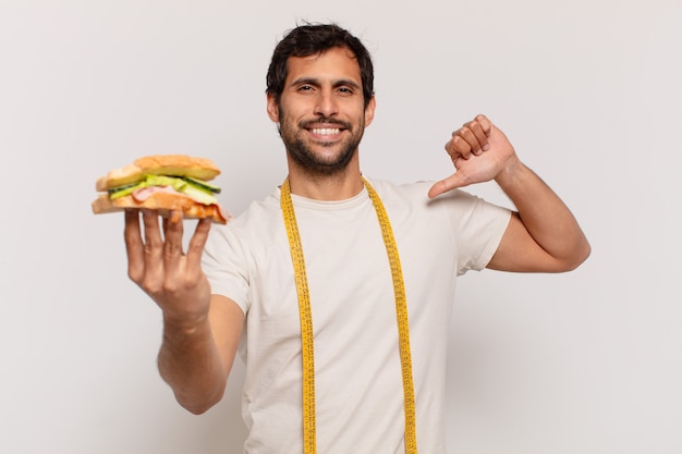 Jovem indiano bonito com expressão feliz e segurando um sanduíche