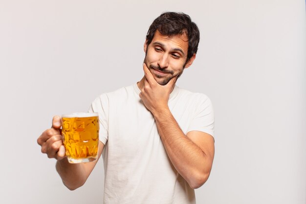 Jovem indiano bonito pensando em expressão e segurando uma cerveja