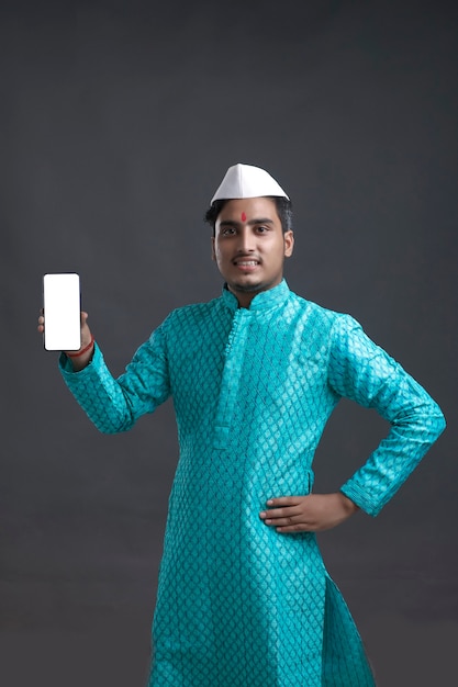 Jovem indiano com roupa tradicional e apresentando smartphone.