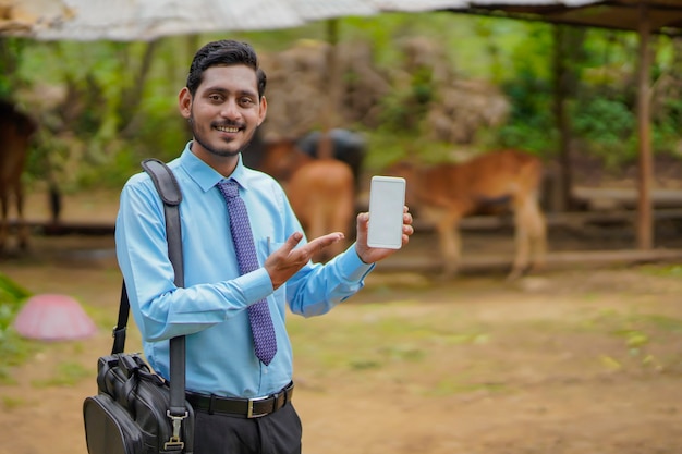 Jovem indiano de banco ou agrônomo mostrando smartphone na casa de fazendeiros