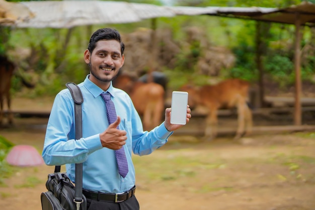Jovem indiano de banco ou agrônomo mostrando smartphone na casa de fazendeiros