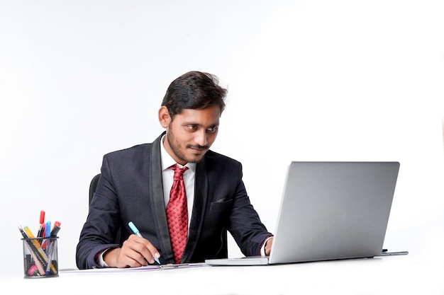 Jovem indiano de terno e trabalhando no laptop e escrevendo uma nota no escritório.