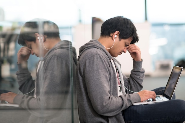 Jovem indiano desenvolvedor de software usando um laptop escrevendo código de programação enquanto está sentado no chão de um moderno escritório criativo