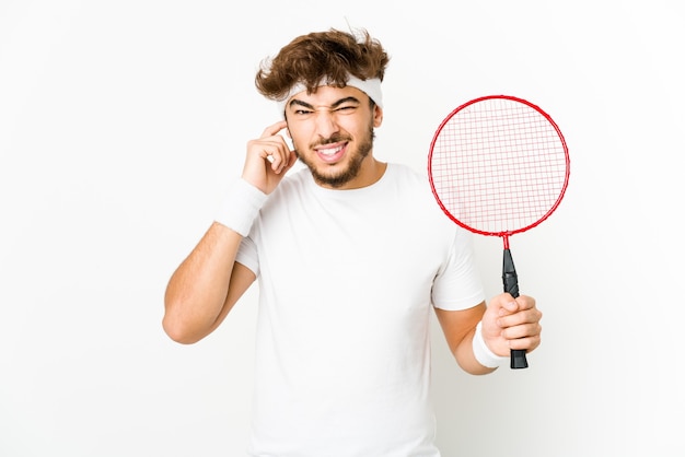 Jovem indiano jogando badminton, cobrindo as orelhas com as mãos.