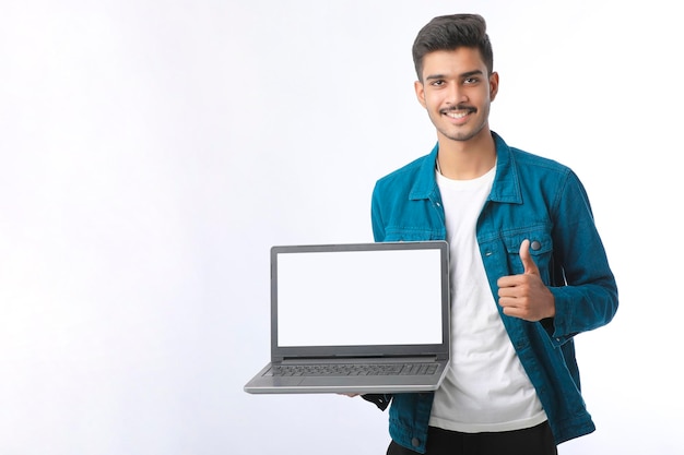 Jovem indiano mostrando a tela do laptop em fundo branco.