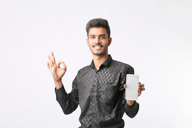 Jovem indiano mostrando a tela do smartphone em fundo branco.