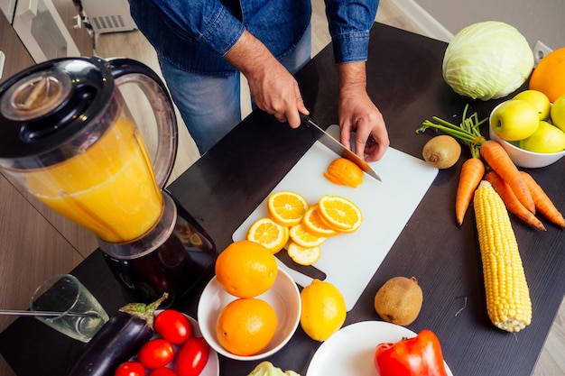 Jovem indiano na cozinha prepara um suco de laranja fresco.