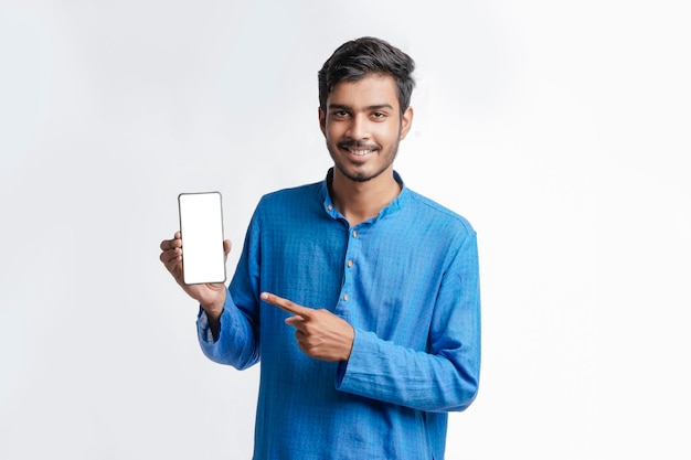 Jovem indiano na roupa tradicional e mostrando a tela do smartphone em fundo branco.