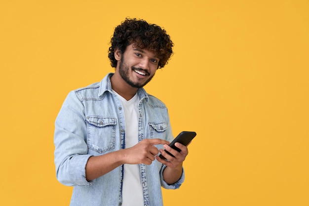 Foto jovem indiano sorridente usando telefone celular isolado em fundo amarelo