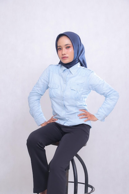 Jovem indonésia mulher de escritório vestindo uma camisa azul hijab sentado em uma cadeira elegante mãos segurando ele