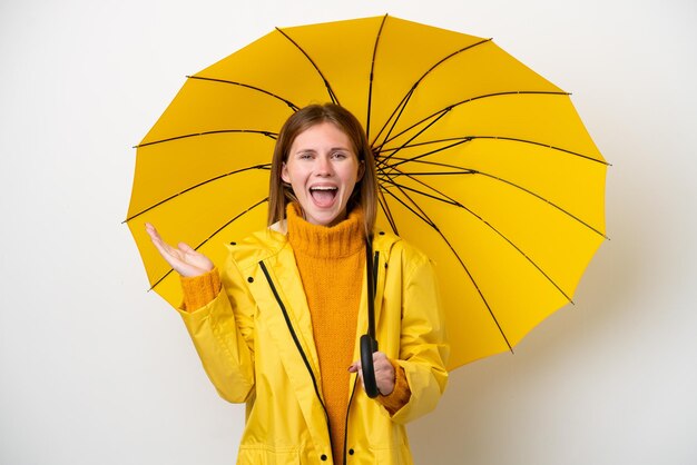 Jovem inglesa com casaco à prova de chuva e guarda-chuva isolado no fundo branco com expressão facial chocada