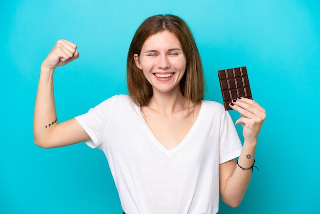 Jovem inglesa com chocolate isolado em fundo azul, fazendo um gesto forte