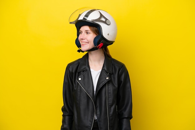 Jovem inglesa com um capacete de moto isolado em fundo amarelo, olhando de lado