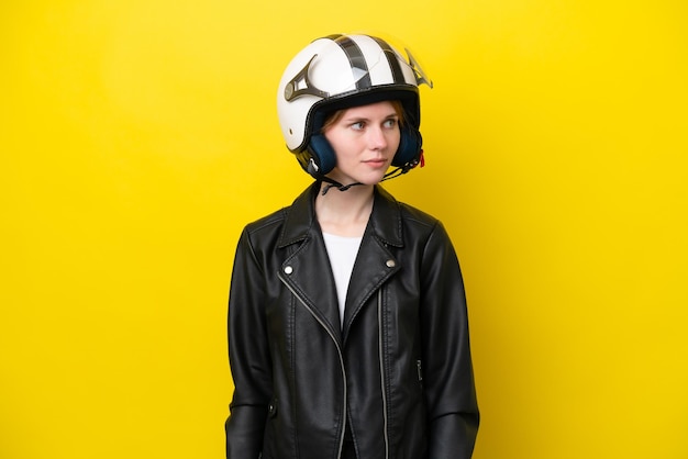 Jovem inglesa com um capacete de moto isolado em fundo amarelo, olhando para o lado