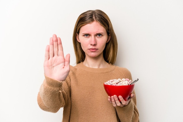 Jovem inglesa comendo cereais isolados em fundo branco de pé com a mão estendida mostrando sinal de pare impedindo você