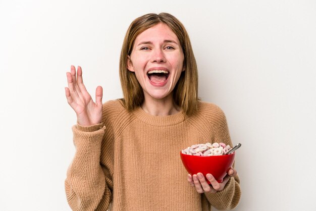 Jovem inglesa comendo cereais isolados no fundo branco recebendo uma agradável surpresa animada e levantando as mãos