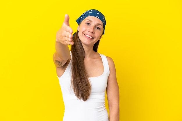 Jovem inglesa isolada em fundo amarelo apertando as mãos para fechar um bom negócio