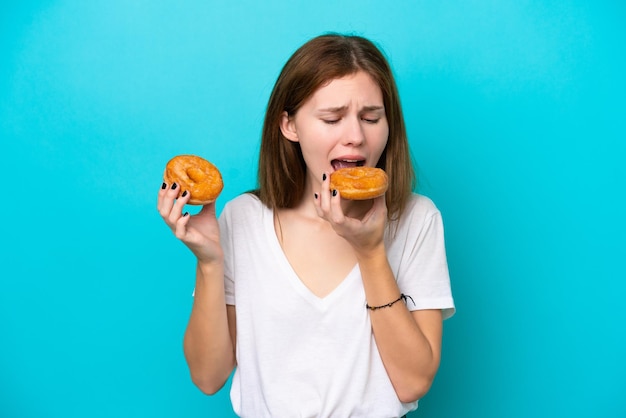 Jovem inglesa isolada em fundo azul comendo uma rosquinha