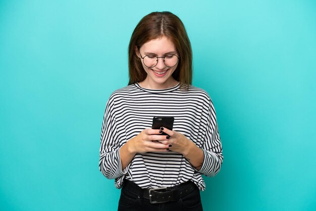 Jovem inglesa isolada em fundo azul enviando uma mensagem com o celular