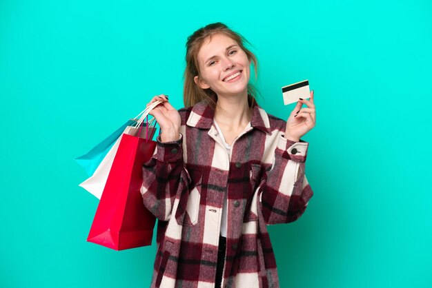 Jovem inglesa isolada em fundo azul segurando sacolas de compras e um cartão de crédito