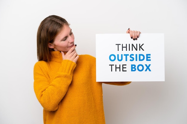 Jovem inglesa isolada em fundo branco segurando um cartaz com texto Think Outside The Box e pensando