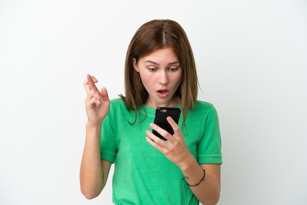 Jovem inglesa isolada em fundo branco usando telefone celular com dedos cruzando