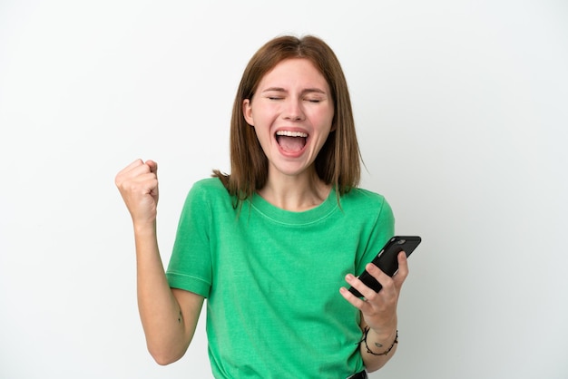 Jovem inglesa isolada em fundo branco usando telefone celular e fazendo gesto de vitória