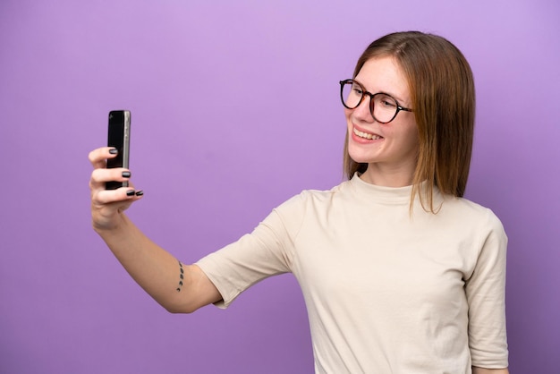 Jovem inglesa isolada em fundo roxo fazendo uma selfie