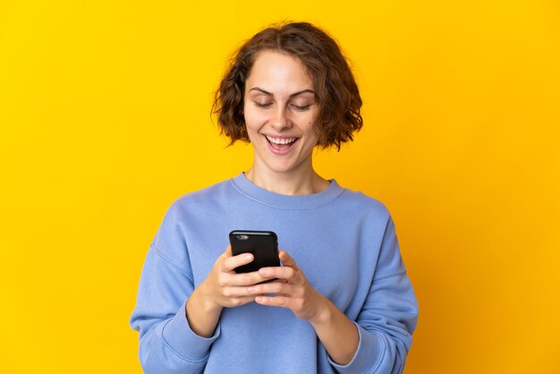Jovem inglesa isolada em uma parede amarela enviando uma mensagem ou e-mail com o celular