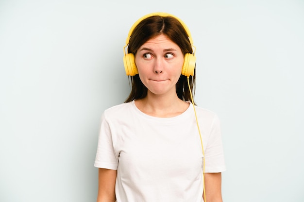 Jovem inglesa ouvindo música isolada em fundo azul confusa sente-se duvidosa e insegura