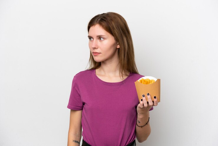 Foto jovem inglesa segurando batatas fritas isoladas no fundo branco, olhando para o lado