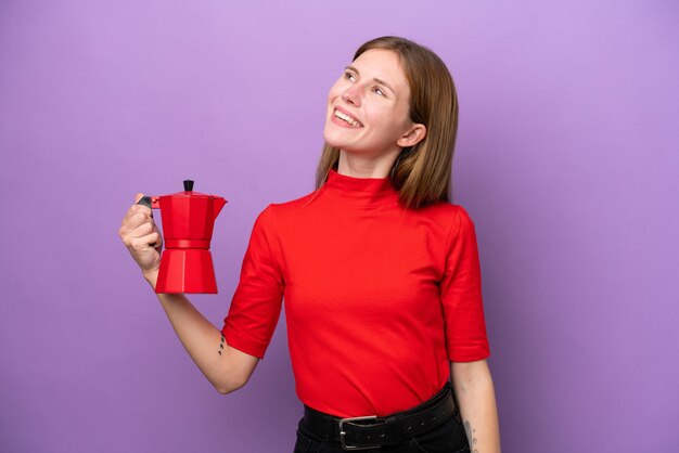 Jovem inglesa segurando o bule de café isolado no fundo roxo olhando para cima enquanto sorria