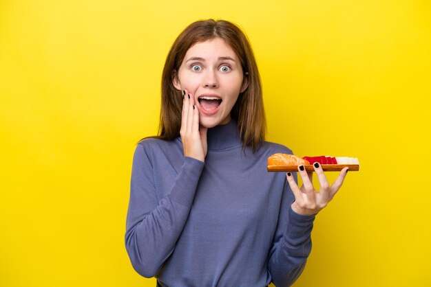 Jovem inglesa segurando sashimi isolado em fundo amarelo com surpresa e expressão facial chocada